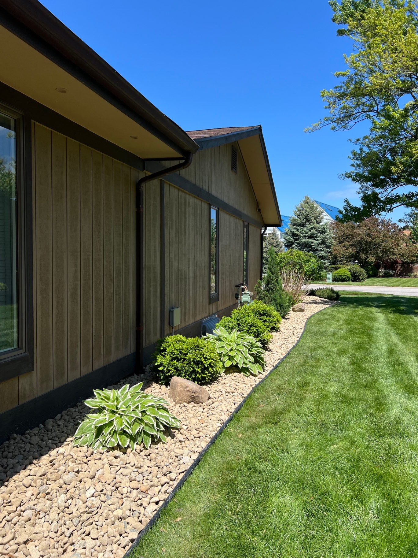 River rock border with hostas and boxwoods along a home