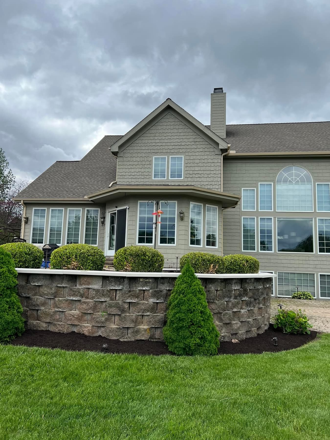Stone retaining wall with trimmed shrubs and fresh mulch beds along a home